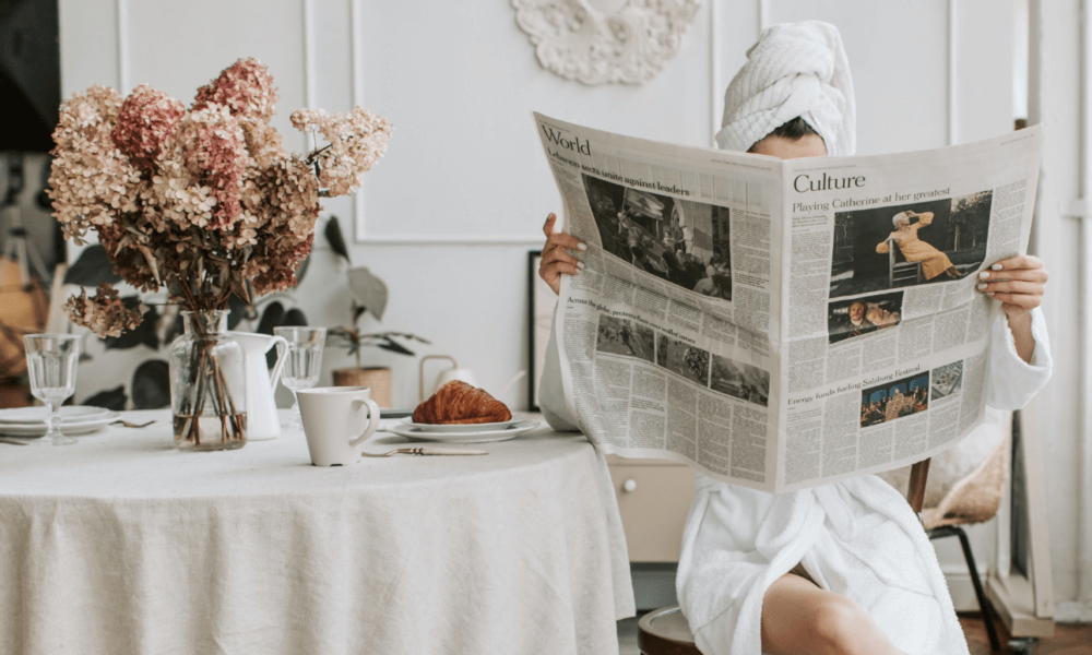 A girl in her bathrobe reading the newspaper at the breakfast table