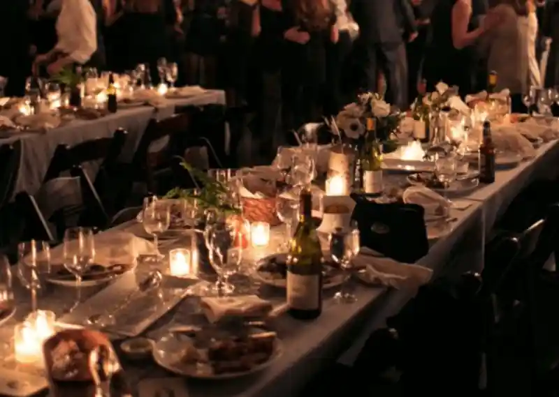 Long dining table full of glasses, plates and some wine bottle