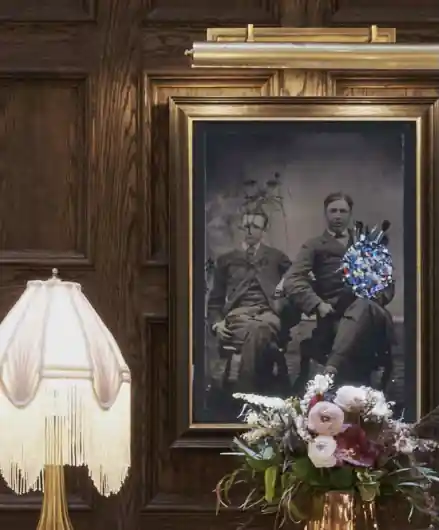 A portrait of two men sitting on the chairs which is hanging just beside the table lamp